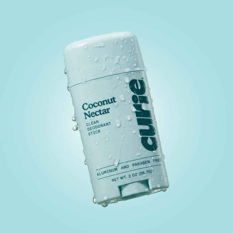 Curie Coconut Nectar Clean Deodorant Stick in a white plastic container with water droplets, set against a light blue gradient background.